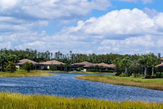 Scenic residential neighborhood with houses along a blue river or lake under a partly cloudy sky.