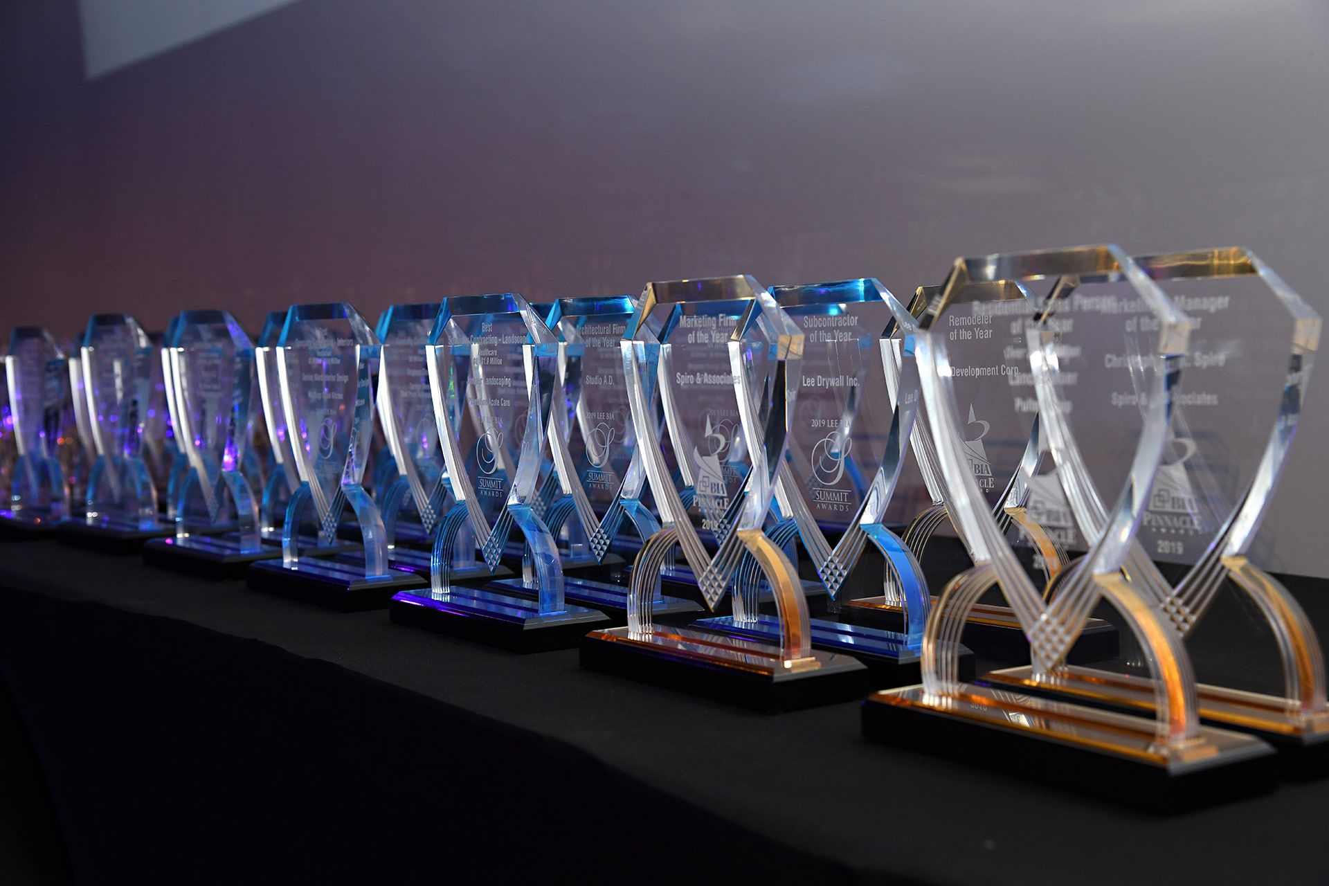 Row of illuminated trophy cups on a display table at an awards event.