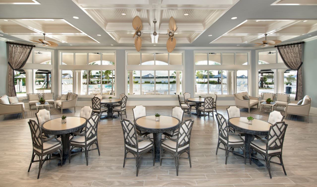 Bright seaside banquet hall with neatly arranged round tables and chairs, large windows, and hanging ceiling lights.
