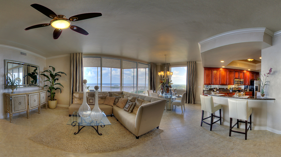Spacious living room with large windows, beige furniture, a ceiling fan, and an open kitchen with bar seating.