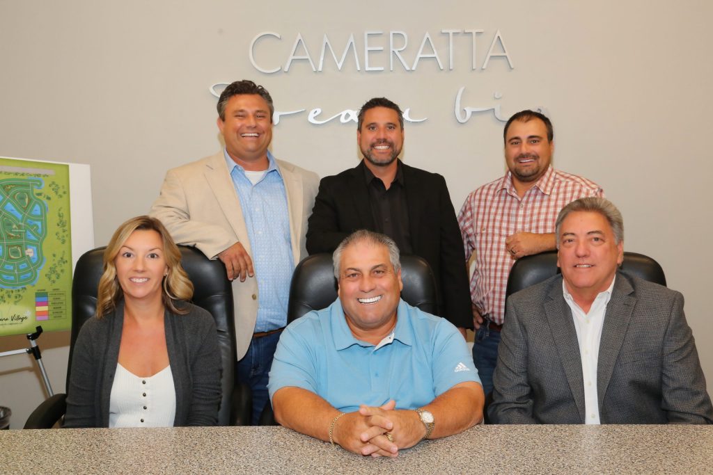Group photo of nine people in front of a “CAMERATTA” banner.