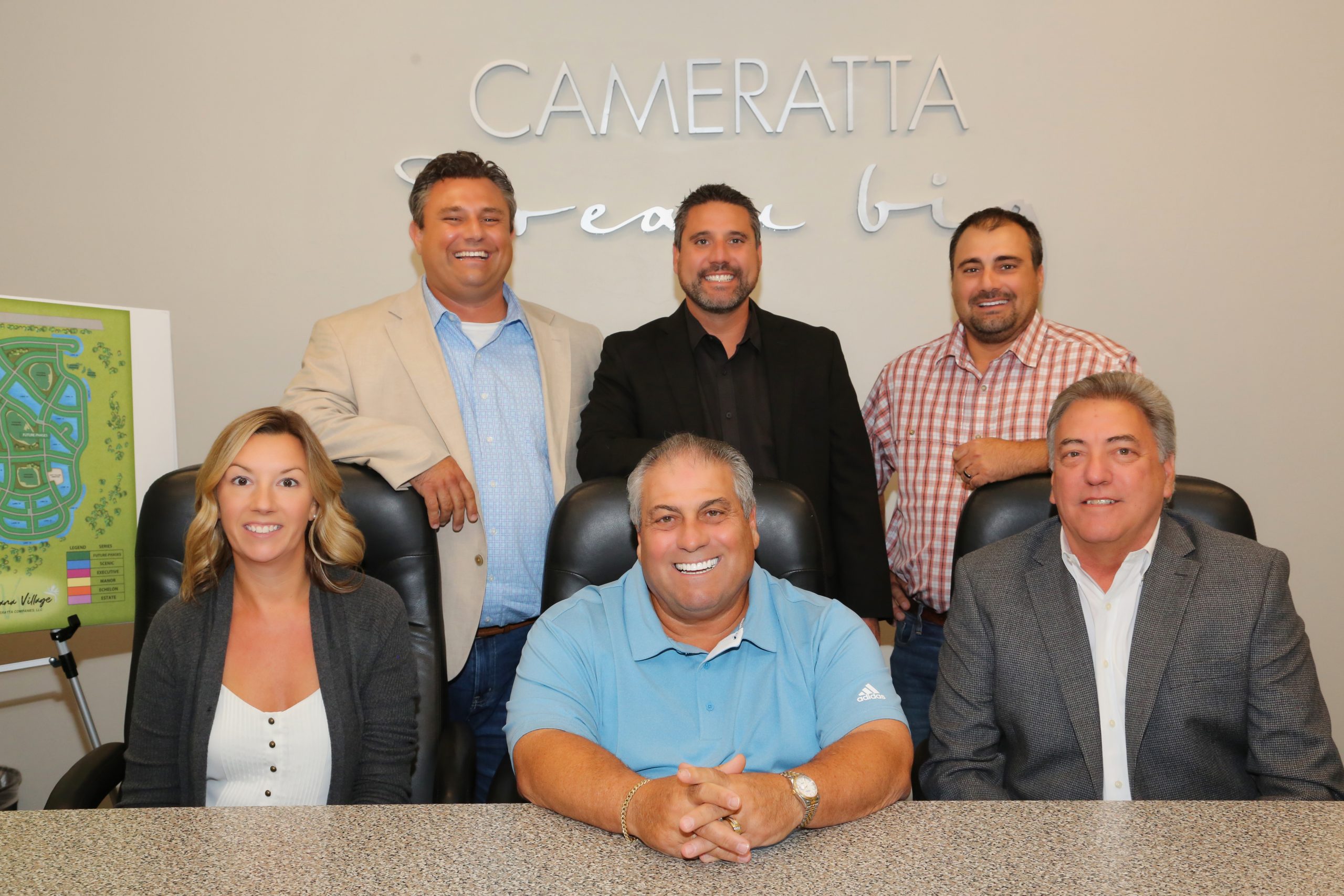Group photo of nine people in front of a “CAMERATTA” banner.