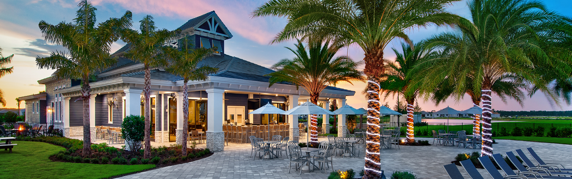 Tropical resort villa with palm trees and a blue-roofed building beside an outdoor seating area.