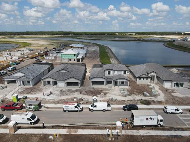 Aerial view of newly built houses beside a large retention pond, with construction vehicles parked along the road.