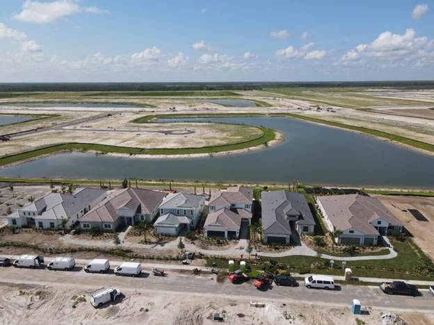Aerial view of homes under construction beside a winding retention pond in a new neighborhood.