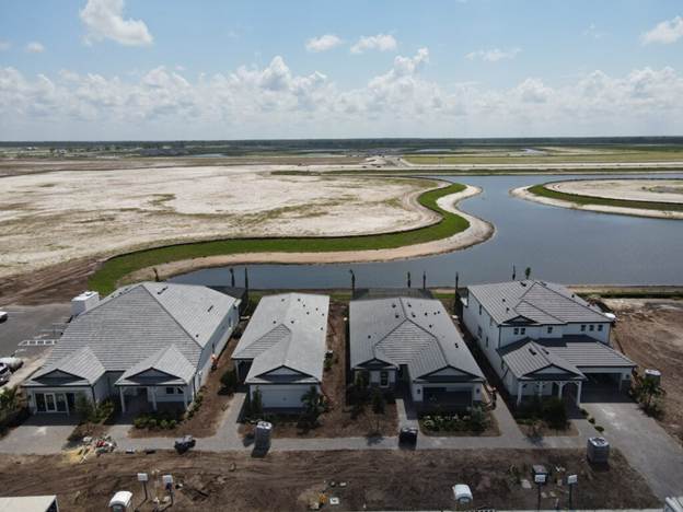 A row of newly built gray-roofed houses overlooks a winding waterway and open marshland.